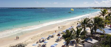 A beach with clear turquoise water, sun loungers, and palm trees.