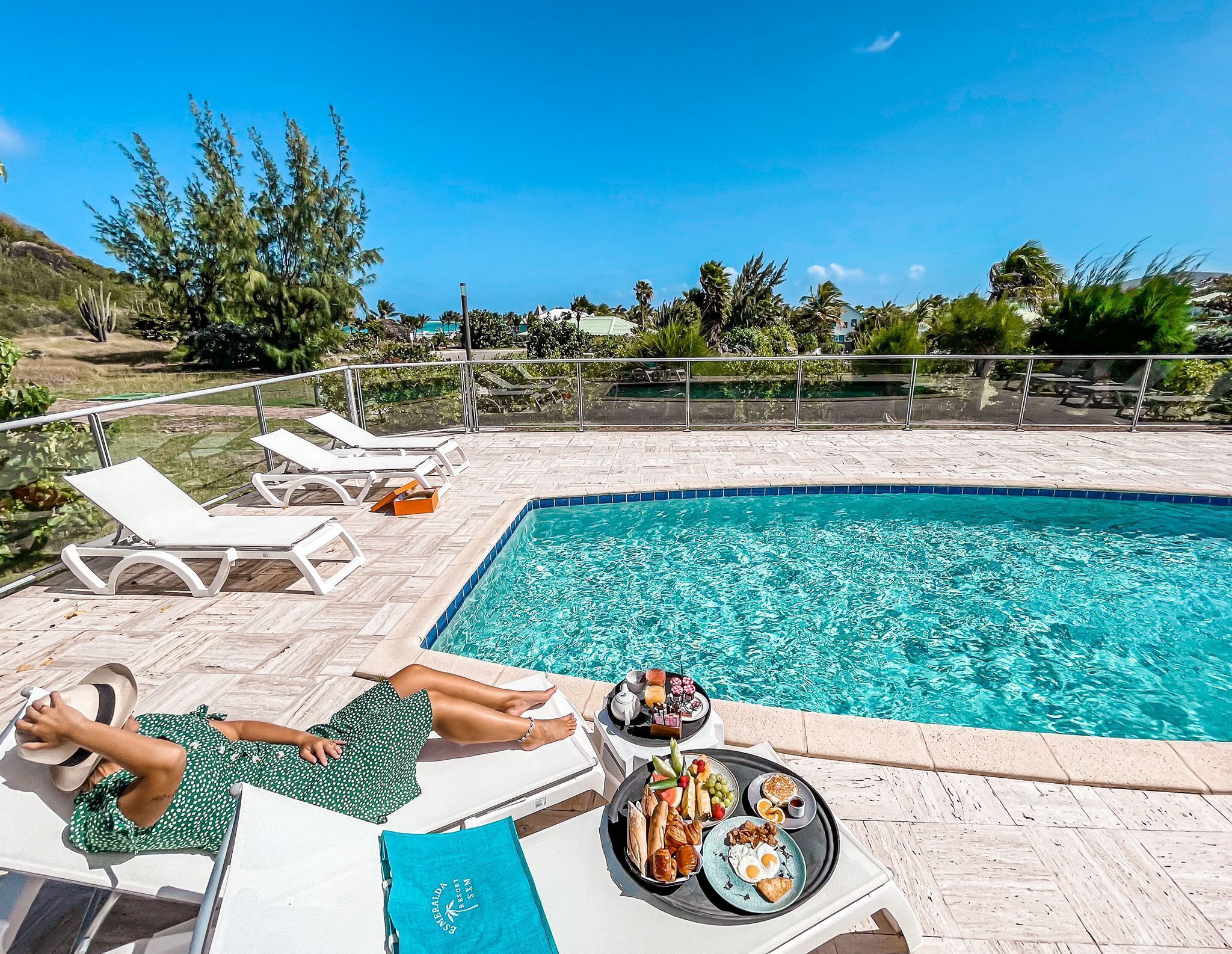 A poolside area with lounge chairs, a dining table with breakfast, and a clear view of the ocean.