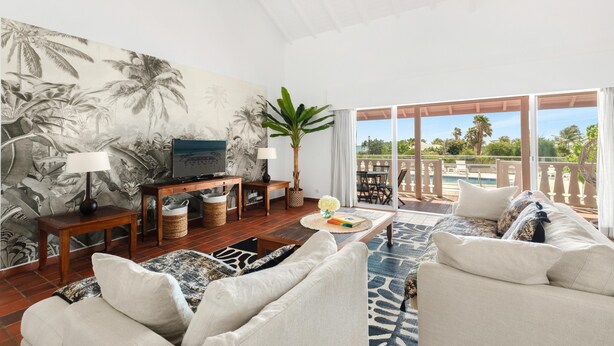 Amplio salón con un gran mural, televisor y balcón con vista a la piscina.