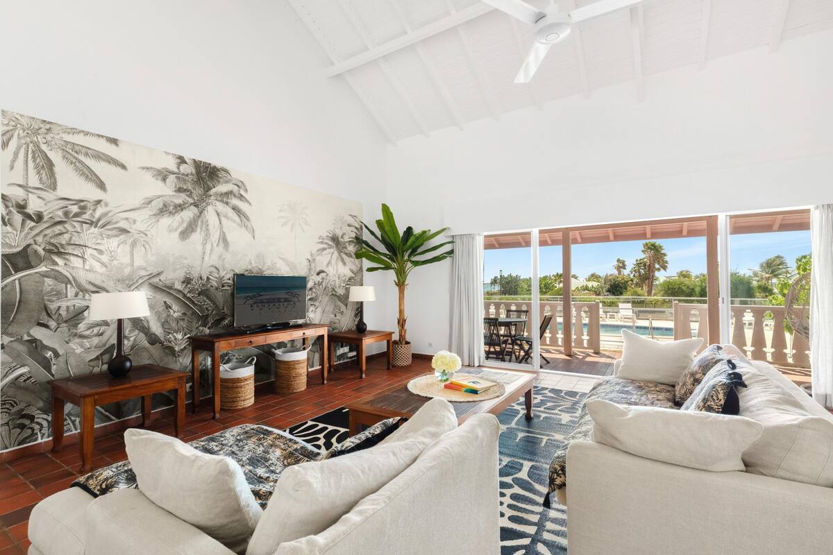 Ein geräumiges Wohnzimmer mit einer großen Wandmalerei, einem Fernseher und einem Balkon mit Blick auf einen Pool.