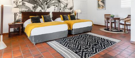 A double bed with a yellow and gray bedspread, a black and white patterned rug, and a large botanical wall art.