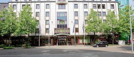 Un hotel moderno con entrada central, varios pisos y un llamativo frente de vidrio.