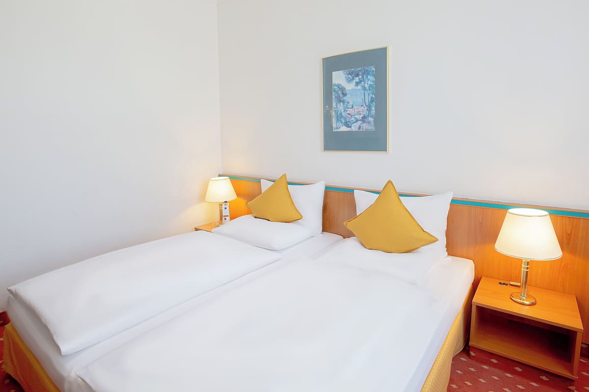 Una habitación de hotel con una cama, dos mesitas de noche, una lámpara y un cuadro en la pared.