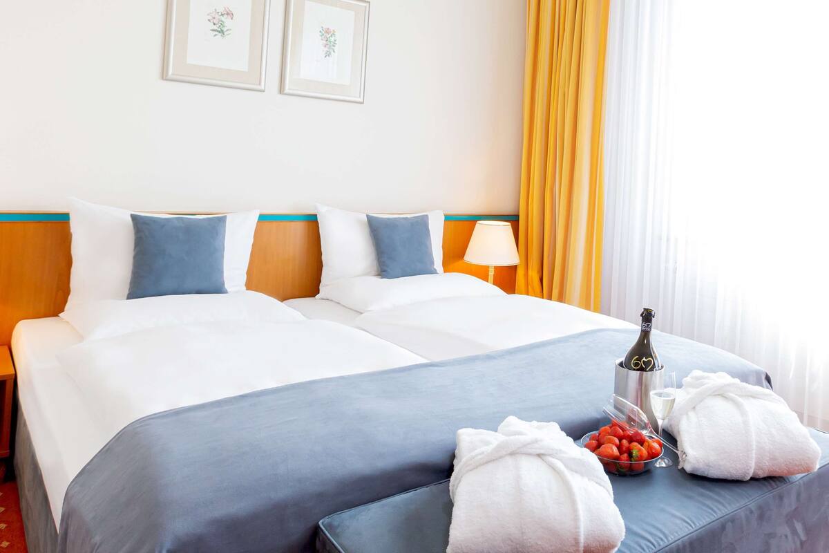 Habitación de hotel con dos camas, una mesita de noche, una lámpara, una botella de champán y un cuenco de fresas.