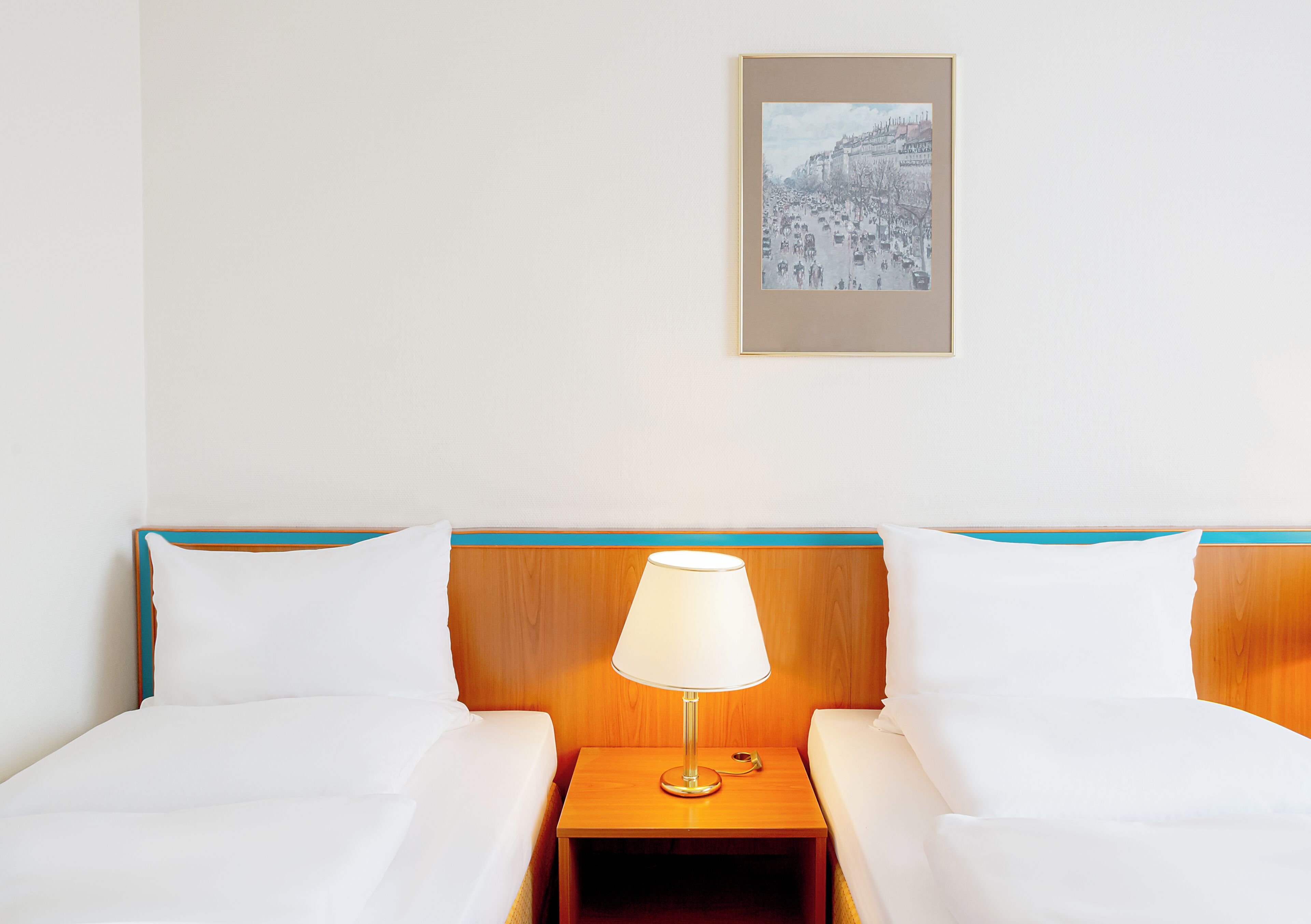 Una habitación de hotel con dos camas, una mesita de noche con lámpara y un cuadro en la pared.