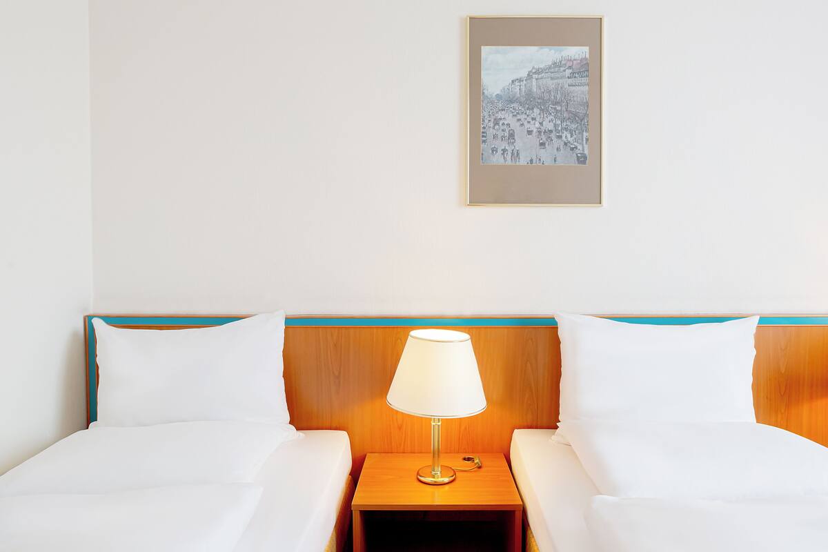 Una habitación de hotel con dos camas, una mesita de noche con lámpara y un cuadro en la pared.