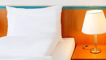 Una cama bien hecha con ropa de cama blanca, un cabecero de madera con detalles en color aguamarina y una mesita de noche con una lámpara.