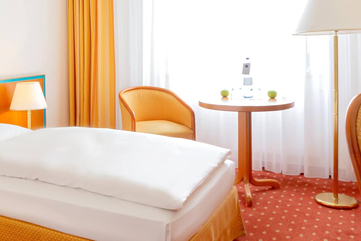 Una habitación de hotel con una cama, una silla, una mesa y una lámpara.