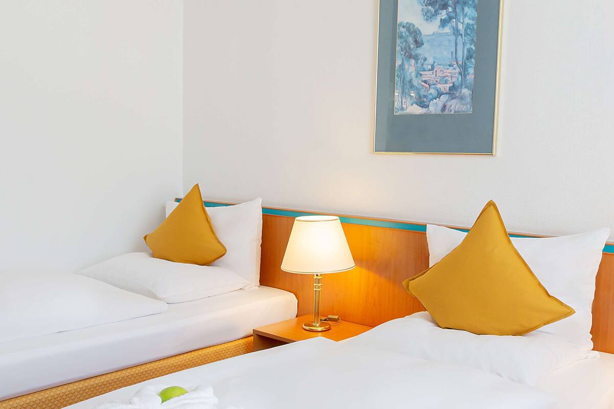 Habitación de hotel con cama, dos almohadas, mesita de noche con lámpara y un cuadro en la pared.
