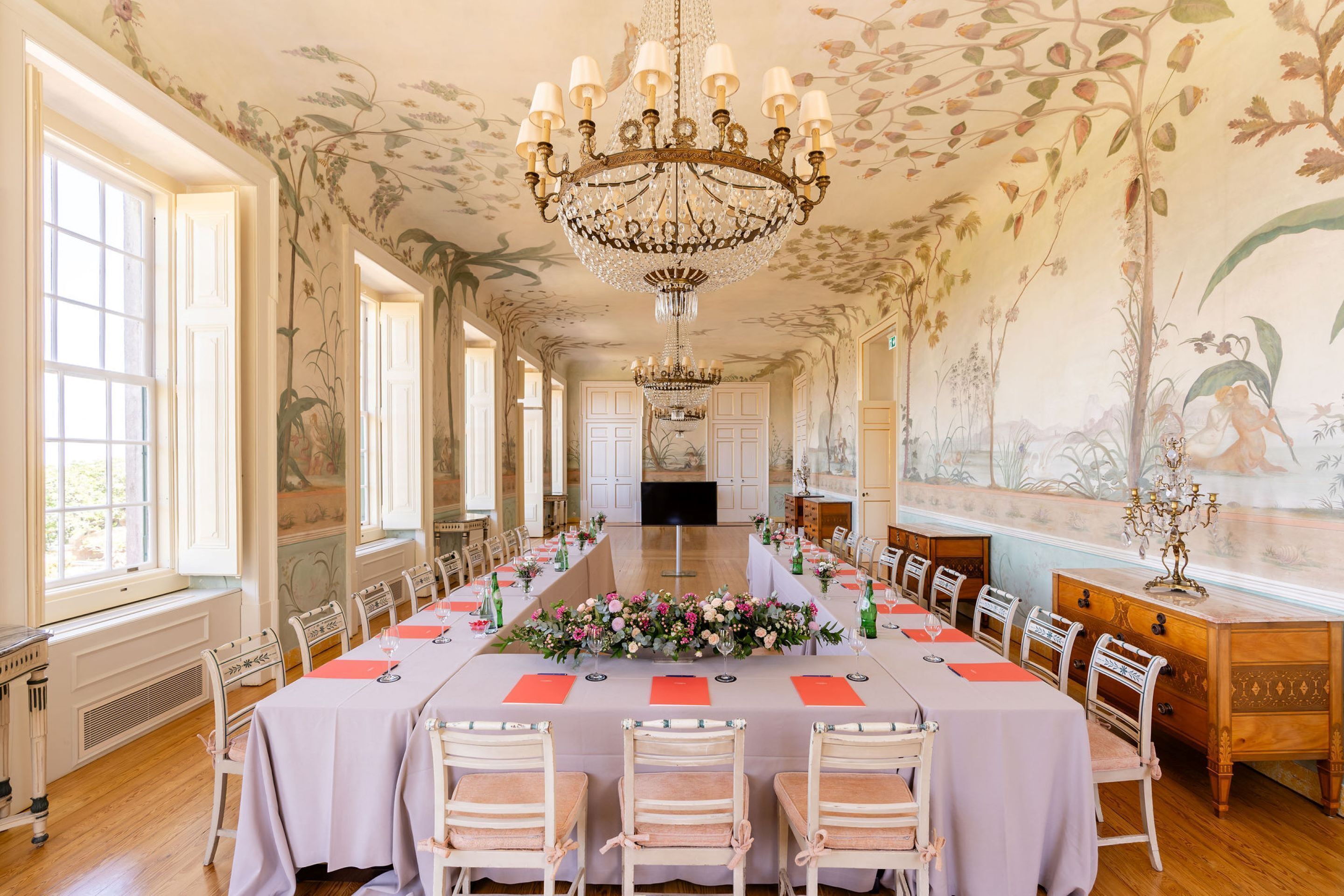 Een lange eettafel gedekt voor een formeel evenement, met stoelen en een bloemstuk.