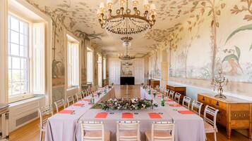 Een lange eettafel gedekt voor een formeel evenement, met stoelen en een bloemstuk.