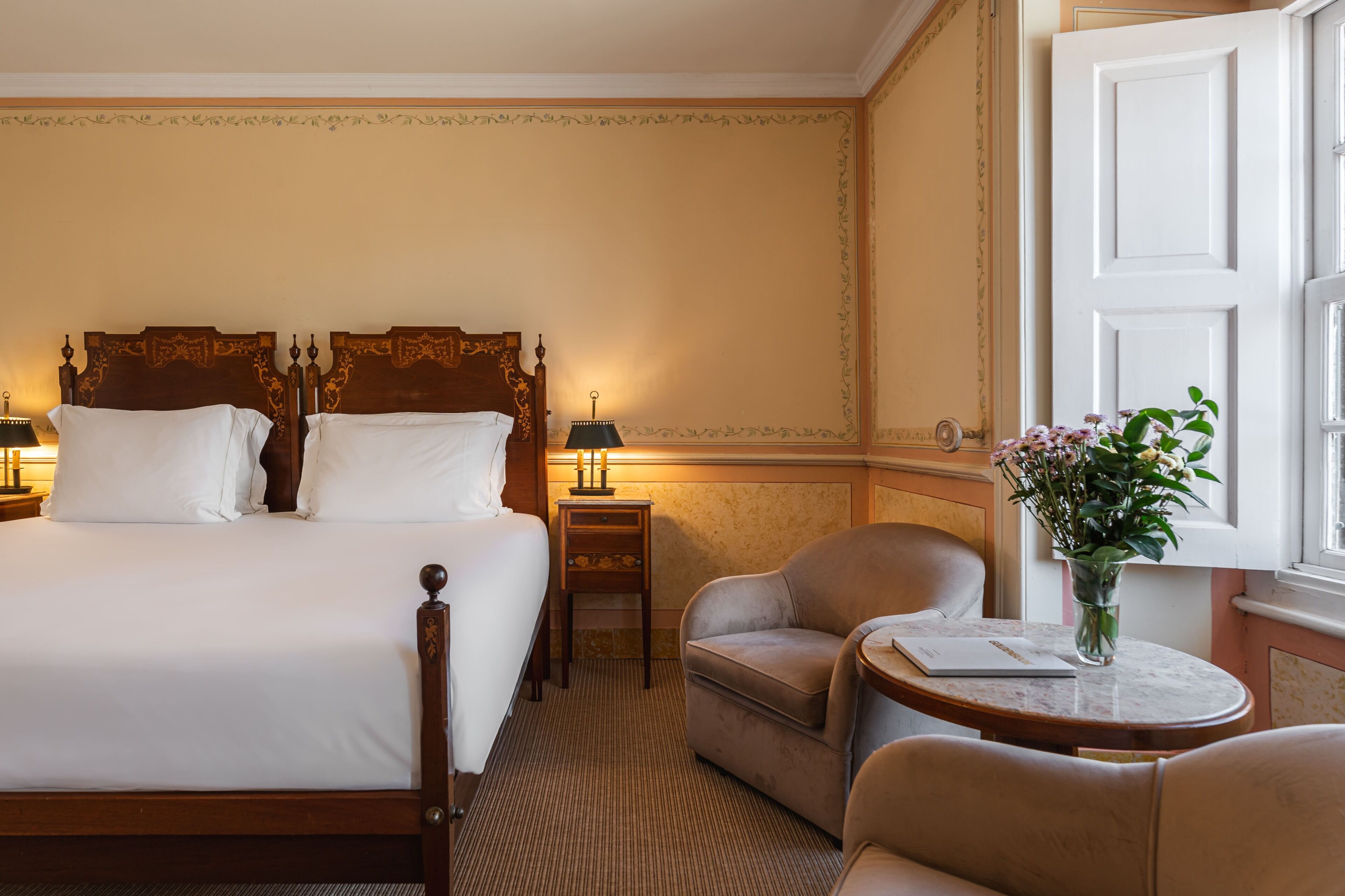 A hotel room with a large bed, two bedside tables, a chair, a small table, and a window with a view.