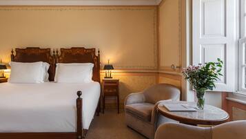 A hotel room with a large bed, two bedside tables, a chair, a small table, and a window with a view.