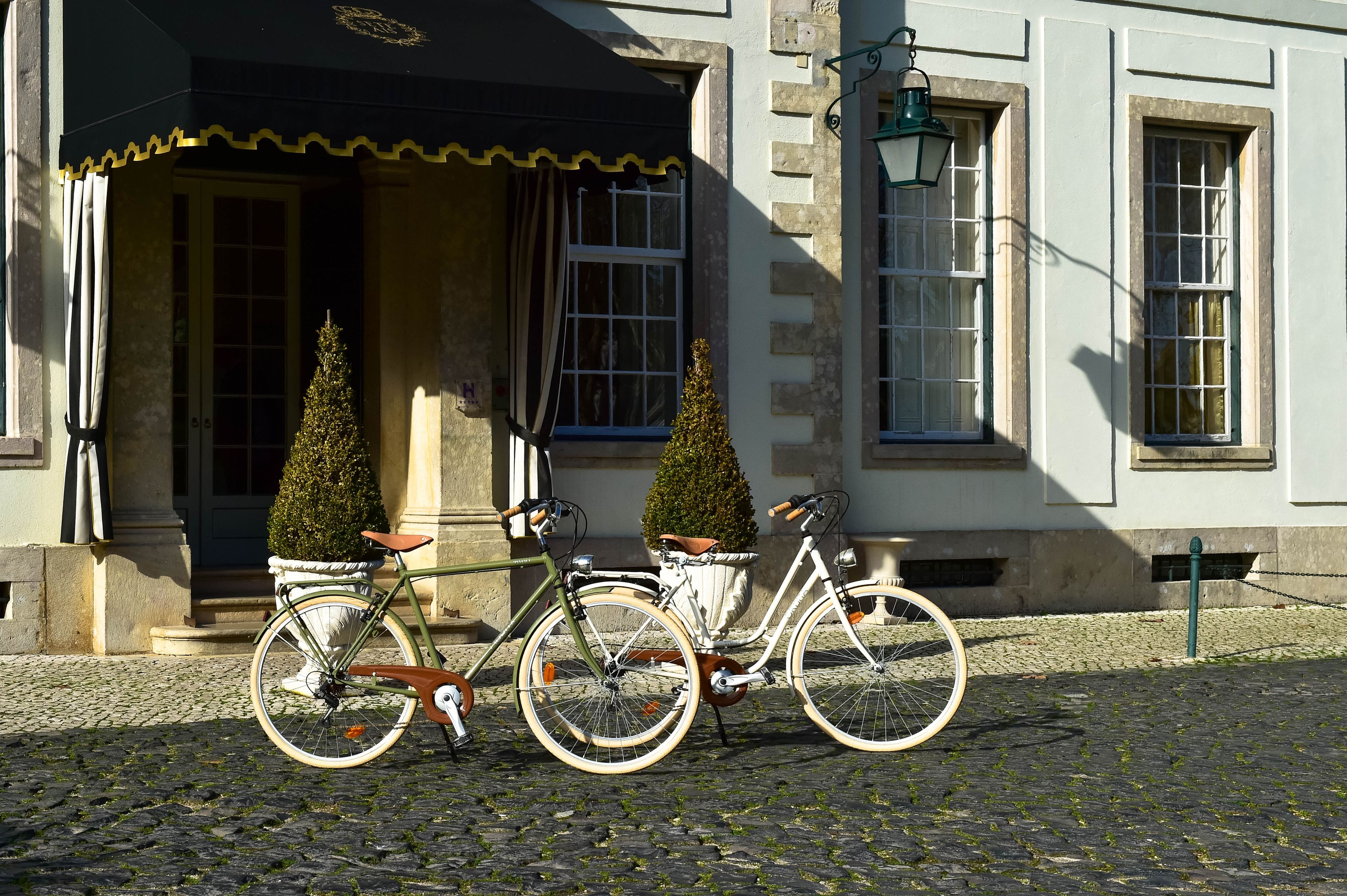 A cobblestone street with two bicycles parked in front of a building with a white facade and a black awning.