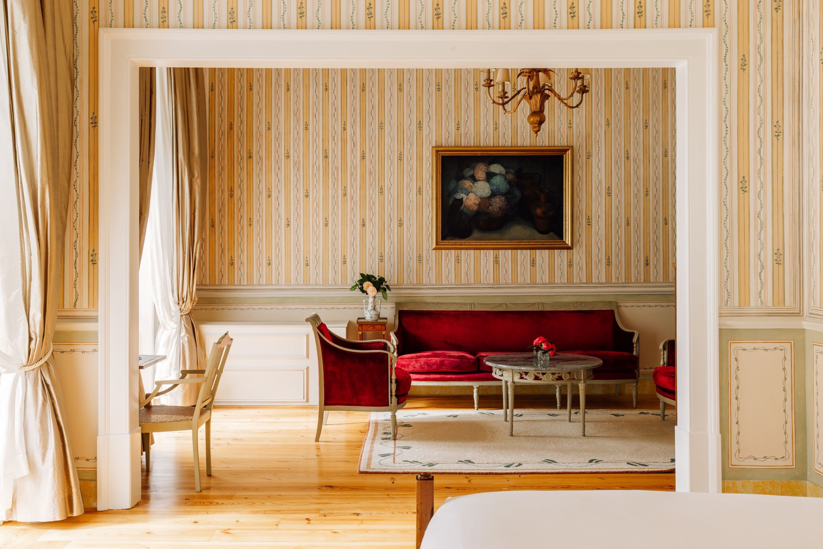 A room with a wooden floor, a red sofa, a small table, and a painting on the wall.