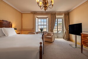 A hotel room with a large bed, a television, a chair, a dresser, and a chandelier.