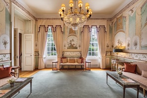 A spacious room with a large chandelier, a sofa, a bench, and a table with a vase of flowers.