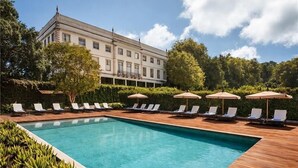 A swimming pool with lounge chairs and umbrellas, surrounded by greenery and a building in the background. - Valverde Sintra Palácio de Seteais - The Leading Hotels of the World (Sintra)