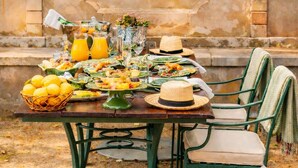 An outdoor dining setup with a stone wall backdrop, a table set with food and drinks, and green metal chairs. - Valverde Sintra Palácio de Seteais - The Leading Hotels of the World (Sintra)