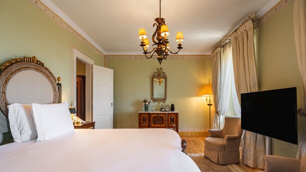 A hotel room with a large bed, a chandelier, a television, a desk, and a chair. - Valverde Sintra Palácio de Seteais - The Leading Hotels of the World (Sintra)
