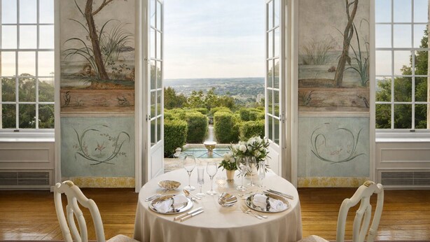 A dining room with a table set for six, large windows, and a view of a garden and cityscape. - Valverde Sintra Palácio de Seteais - The Leading Hotels of the World (Sintra)