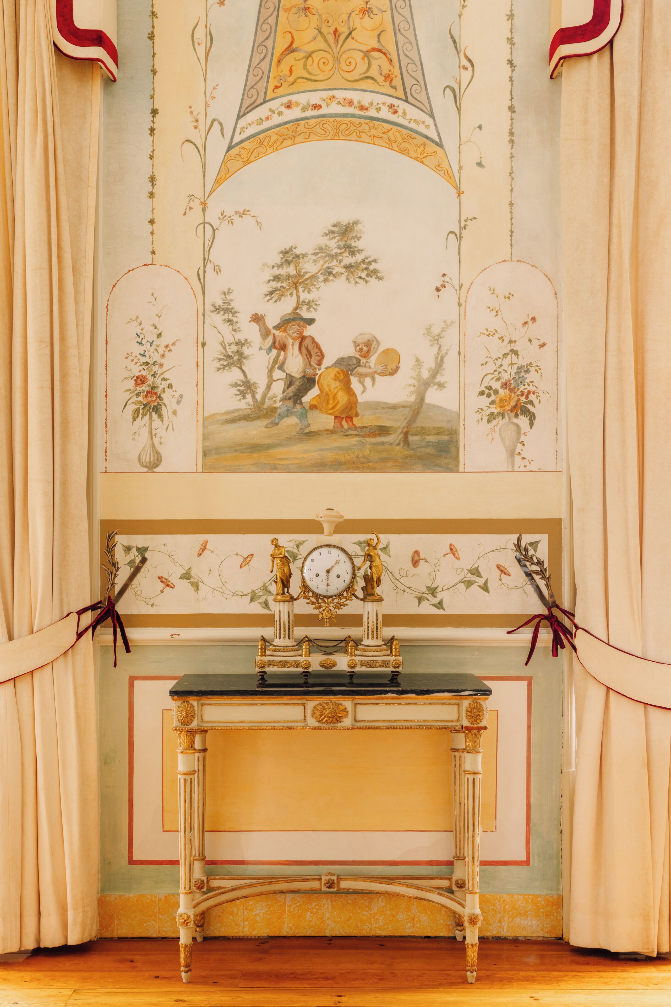 A room with a decorative wall, a clock, and a table with a vase.