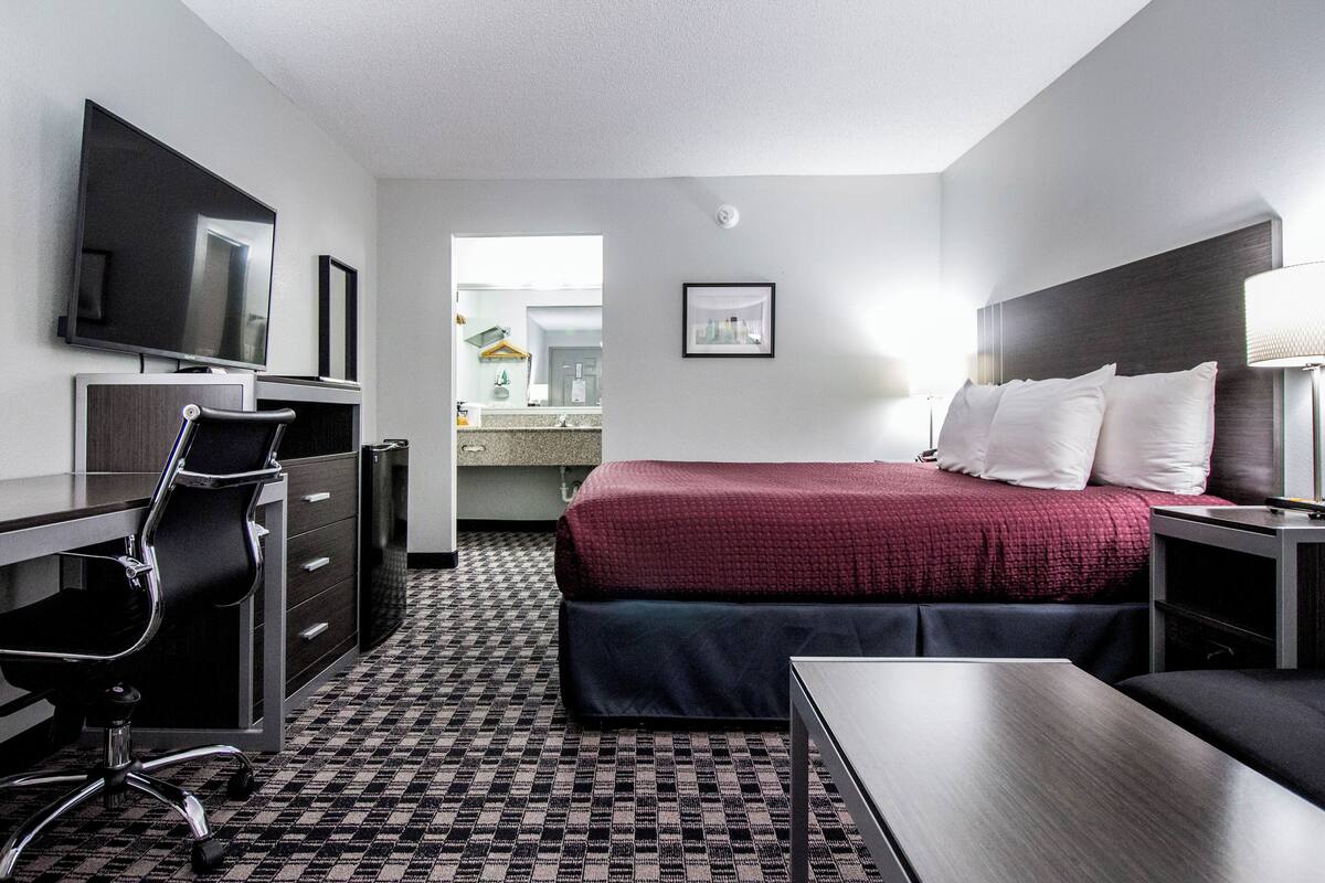 A hotel room with a bed, desk, chair, TV, and a bathroom visible through an open door.