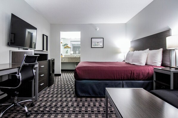 A hotel room with a bed, desk, chair, television, and a bathroom visible through an open door. - Brick Lodge Atlanta/Norcross (Norcross)