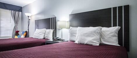 A hotel room with two beds, a nightstand, a lamp, and a window with curtains.