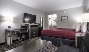 A hotel room with a bed, desk, chair, television, and a bathroom visible through an open door. - Brick Lodge Atlanta/Norcross (Norcross)