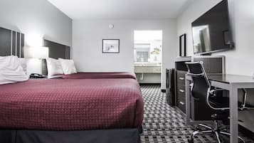 Habitación de hotel con dos camas, un escritorio, una silla, un televisor y un baño visible a través de una puerta abierta.