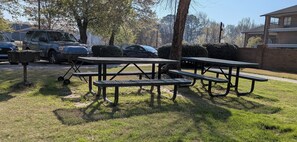 A picnic area with metal tables and benches, surrounded by grass and trees. - Brick Lodge Atlanta/Norcross (Norcross)