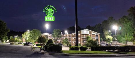 A hotel with a well-lit parking area, multiple floors, and a prominent sign indicating guests charge is free.