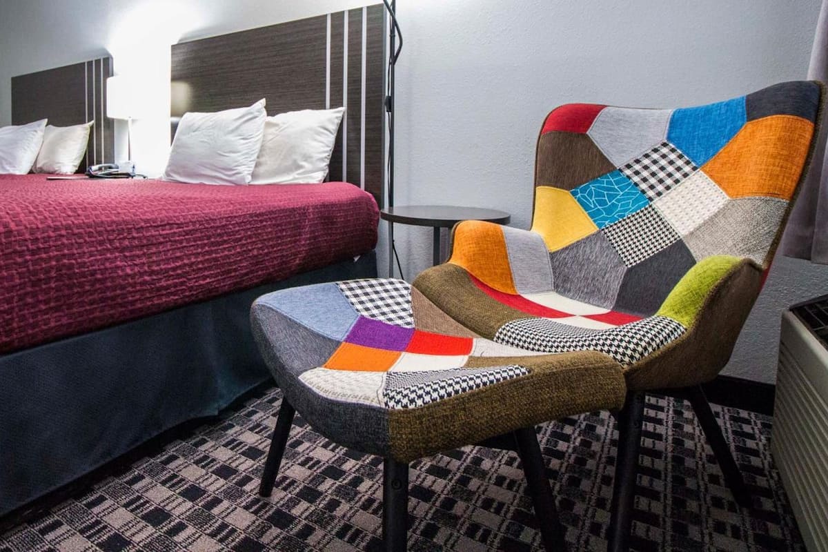 A hotel room with a bed, a chair with a patchwork design, and a patterned floor.