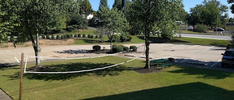 A parking area with a volleyball net, trees, and a picnic table.