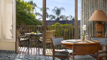 A balcony with wicker furniture, a table with a vase, and a view of trees and buildings.