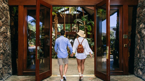 A couple walking through a wooden door into a building with a tropical garden view. - Catamaran Resort and Spa (San Diego)