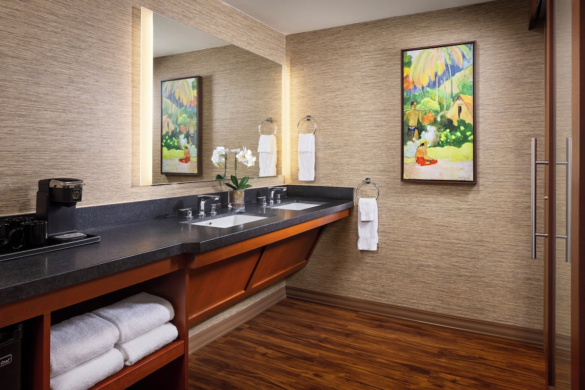 A modern bathroom with a wooden vanity, two sinks, a large mirror, and artwork on the walls.