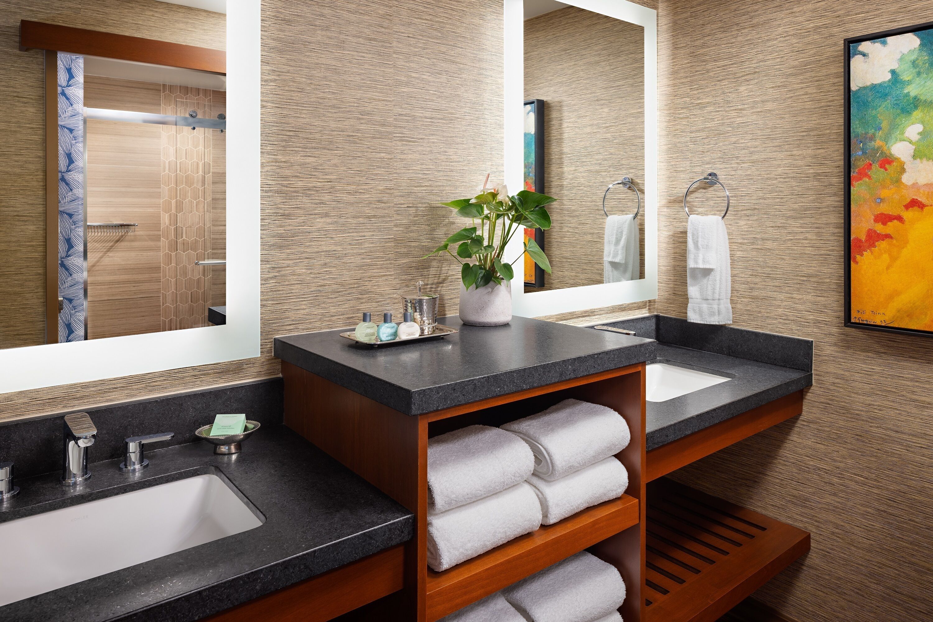 A modern bathroom with two sinks, a large mirror, and a potted plant.