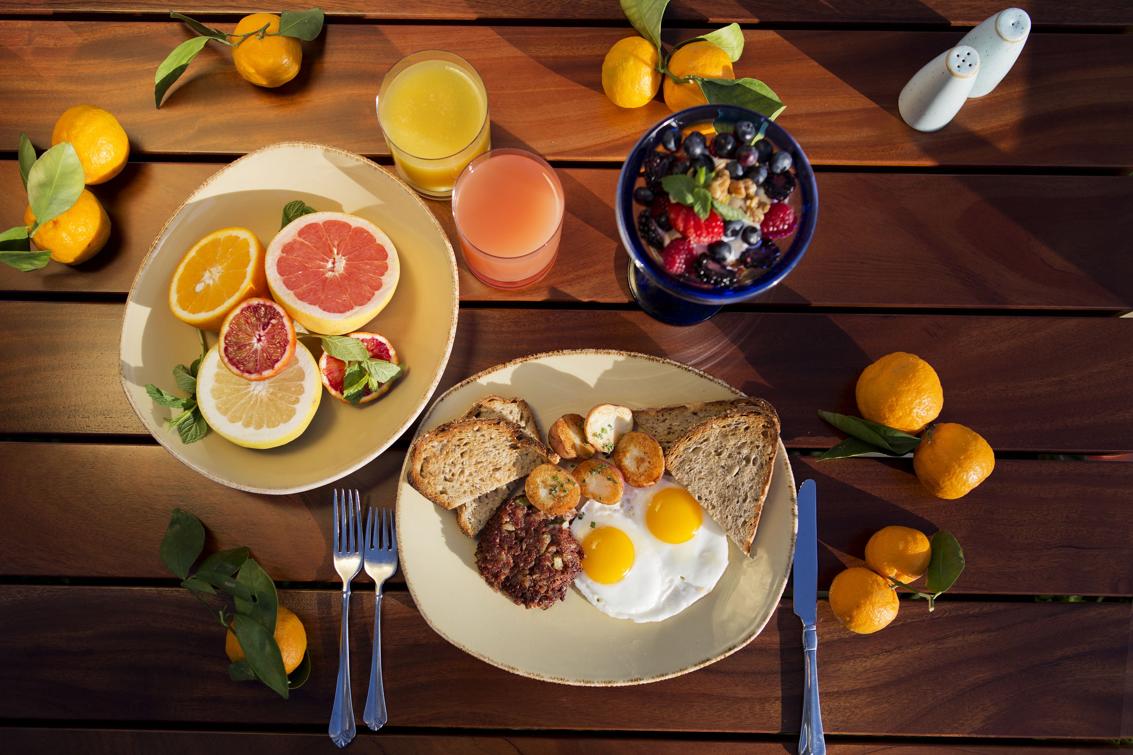 A breakfast setting with plates of food, including toast, eggs, and fruit, on a wooden table.