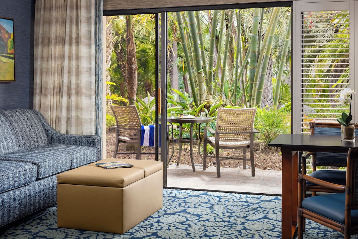 A living room with a sofa, ottoman, and a dining area with chairs and a table.