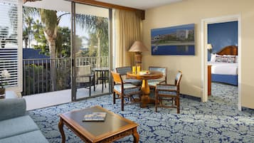 A hotel room with a balcony, a dining area with chairs and a table, a sofa, and a bed.