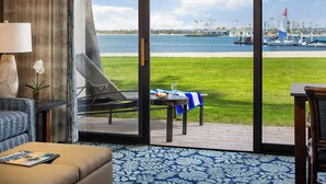A room with a large glass door leading to a grassy deck with a table and chairs, overlooking a marina with boats and a clear sky. - Catamaran Resort and Spa (San Diego)