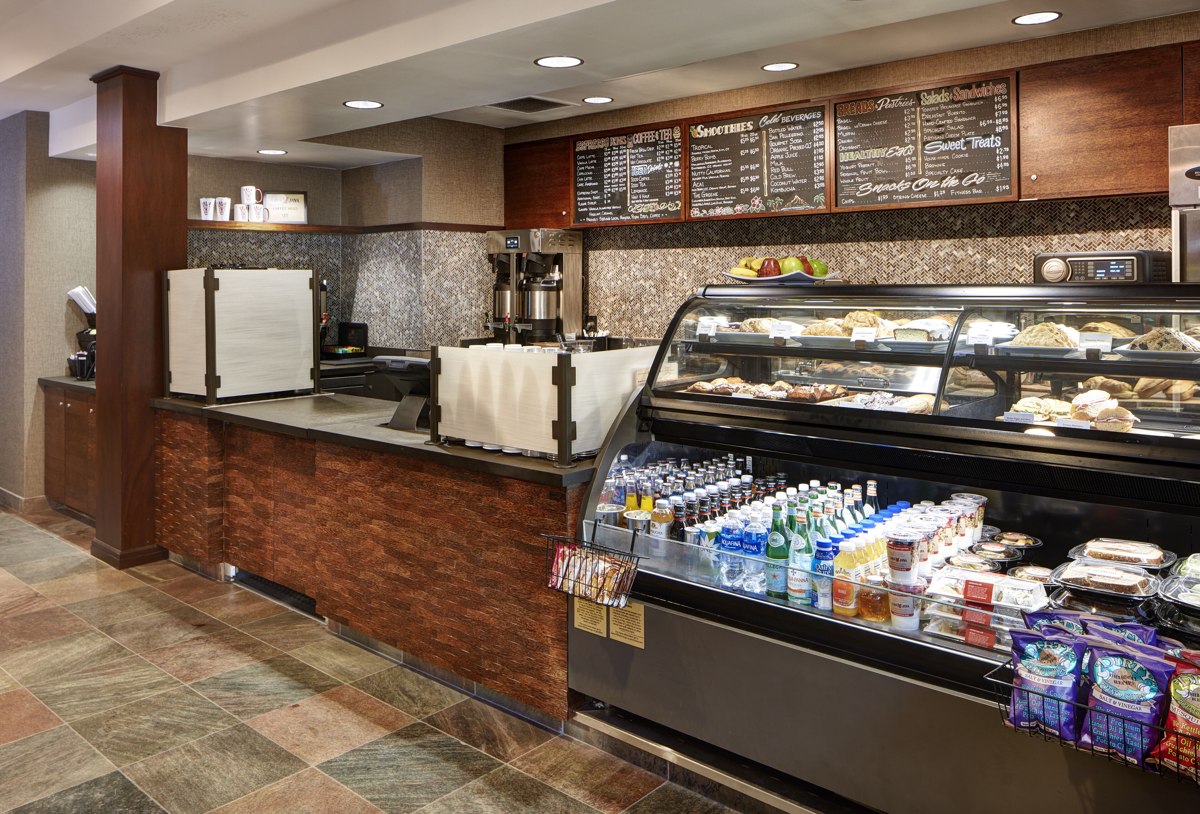 A self-service breakfast area with a variety of food items, a coffee machine, and a refrigerated display case.