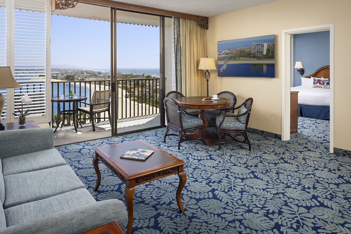 A hotel room with a balcony, a dining area, a bed, and a view of the ocean.