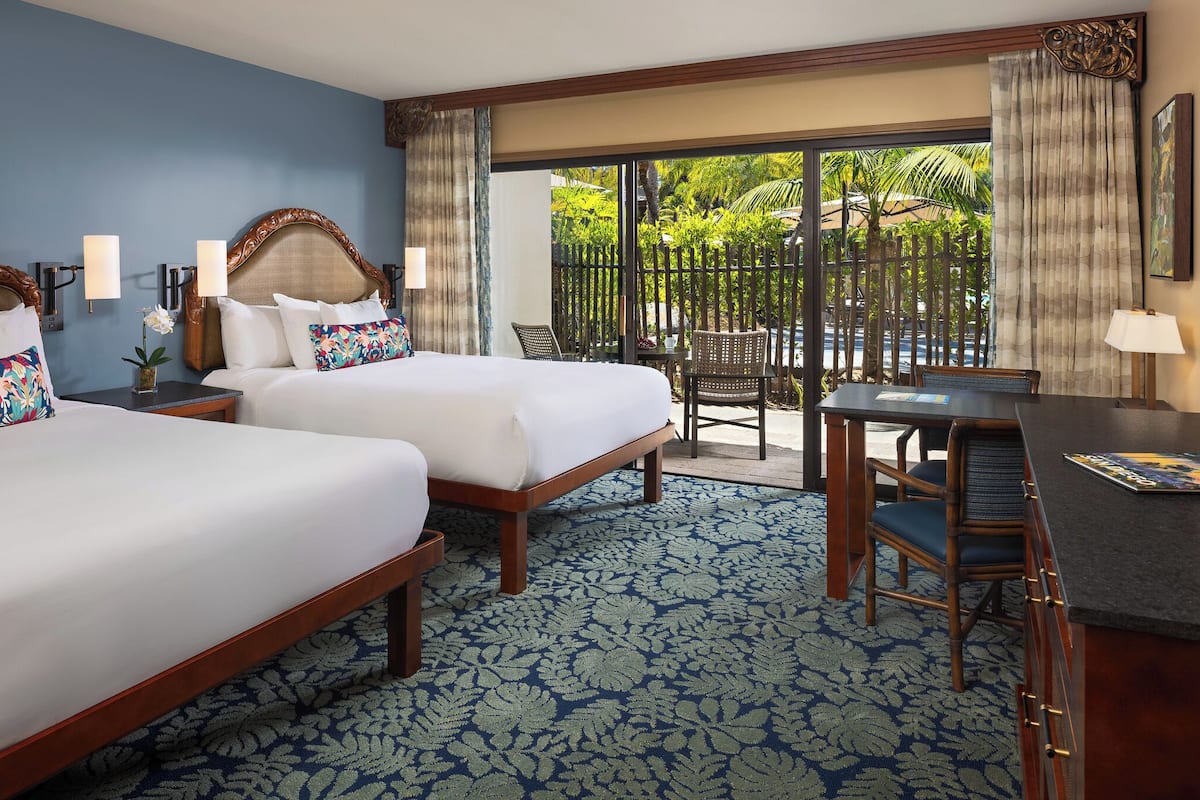 A hotel room with two beds, a desk, and a view of a tropical outdoor area.