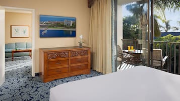 Quarto de hotel com uma cama grande, cómoda de madeira, quadro pendurado na parede, varanda com mesa e cadeiras, e vista para o exterior.