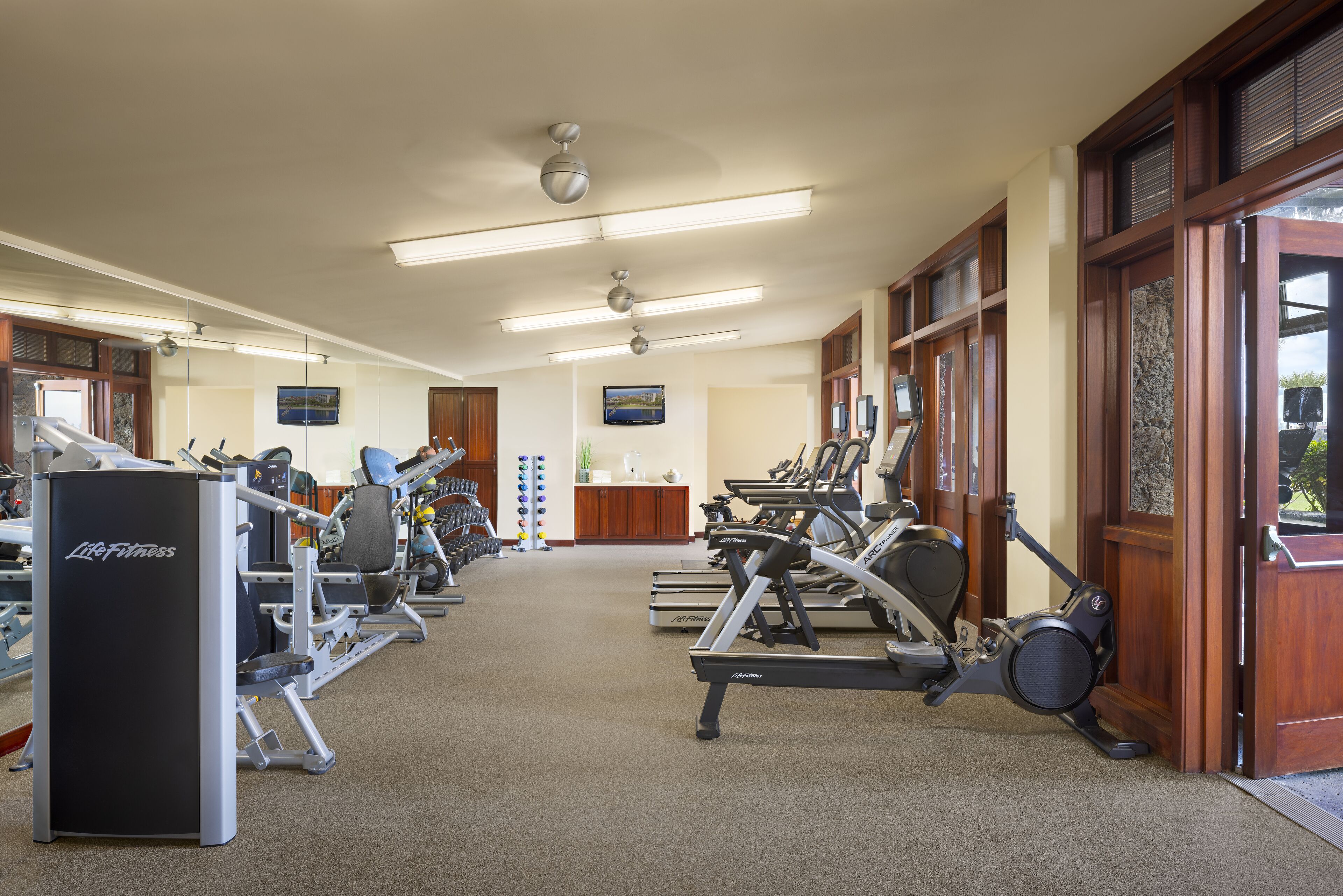 Une salle de sport équipée de divers appareils d’exercice, un comptoir d’accueil et une vue sur l’extérieur grâce à de grandes fenêtres.