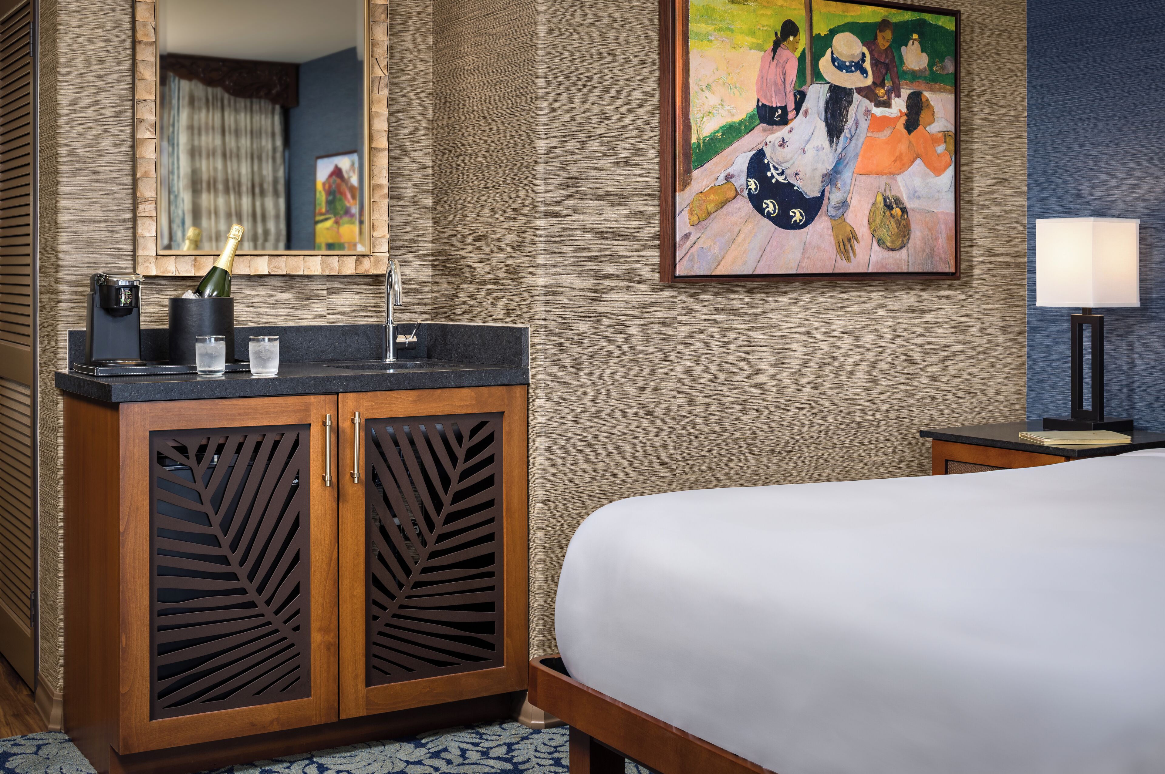 A hotel room with a wooden cabinet, a bed, a nightstand, a lamp, and a painting on the wall.