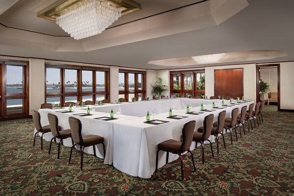 A conference room with a long table, chairs, and large windows overlooking a body of water.